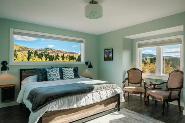 A cozy bedroom featuring large windows with a scenic view of mountains and lush trees outside.
